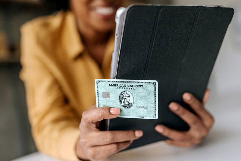 Person holding tablet with American Express business card prominently displayed in foreground.